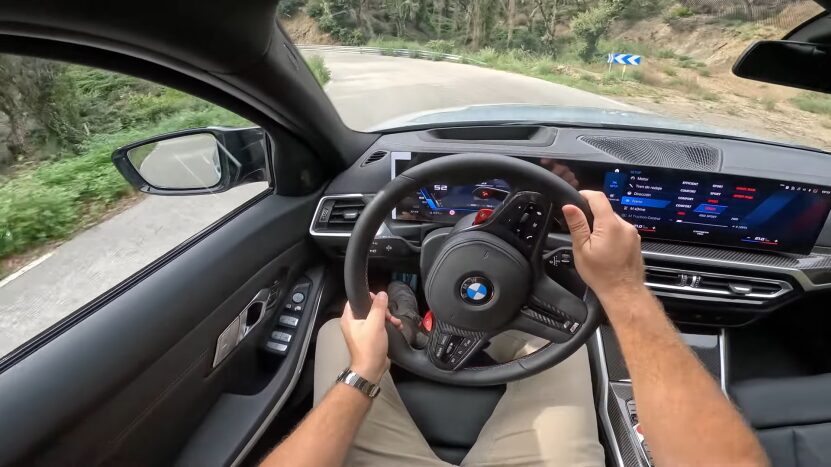 Driver's Perspective Inside the 2025 BMW M5, Showing Hands on The Steering Wheel and The Dashboard with Active Driving Displays While on A Curvy Road