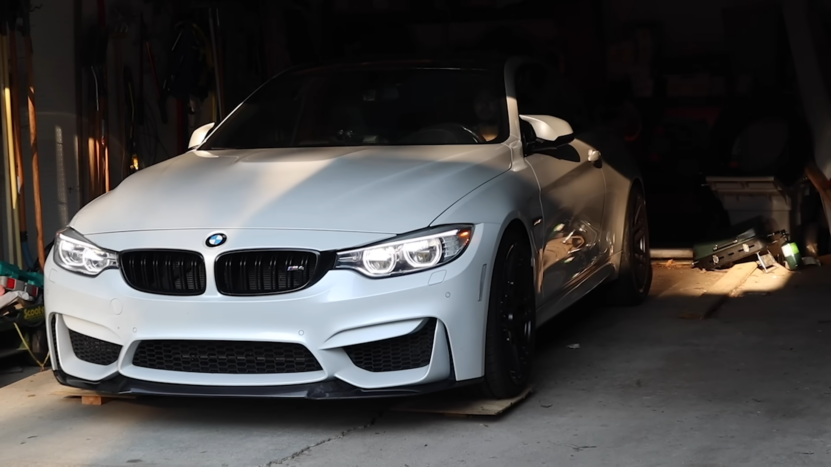 A White BMW M4 Convertible Is Parked in A Garage, with Its Headlights On, Showcasing Its Sleek and Aggressive Front Design