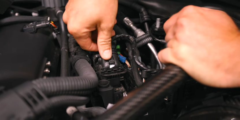 Person Adjusting a Component Inside a BMW Engine Bay During a Car Tune-Up