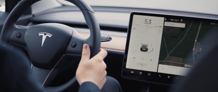 A Driver's Hands on The Steering Wheel of A Tesla, Featuring the Car's Digital Dashboard Displaying Speed and Navigation