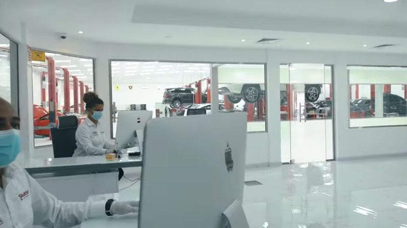 Mechanics and Customer Service Representatives Working in A Pristine, High-Tech Automotive Service Center with Cars on Lifts Visible Through Large Windows