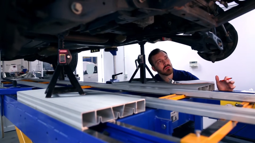 A Mechanic Is Inspecting the Underside of A Car on A Lift to Assess the Damage After a Car Accident