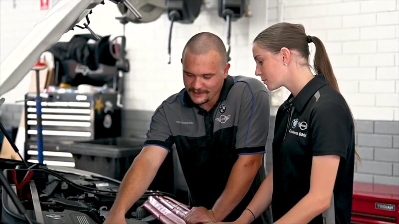 Two BMW Technicians, a Man and A Woman, Working Together on A Car's Engine in A Service Center