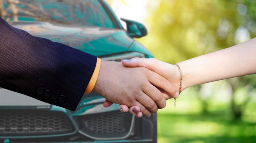 A Man in A Business Suit Shakes Hands with A Woman Over the Hood of A BMW in A Lush, Green Park, Symbolizing the Successful Sale of The Car, Which Was Likely Boosted by Strategic Steps Taken to Maximize the Resale Value of The BMW