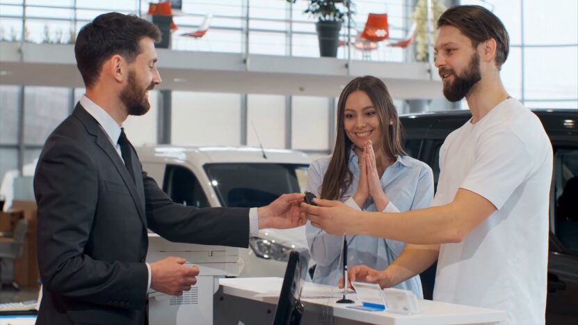 A Salesperson Hands Over Car Keys to A Couple, Symbolizing the Purchase of A New Car