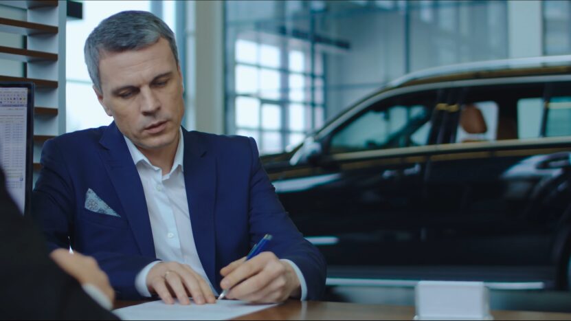 Man Signing Paperwork at A Car Dealership, Potentially Finalizing a Car Lease