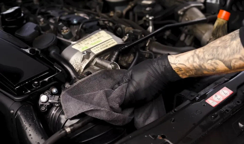 Guy with black gloves cleans car's engine bay with cloth and chemicals